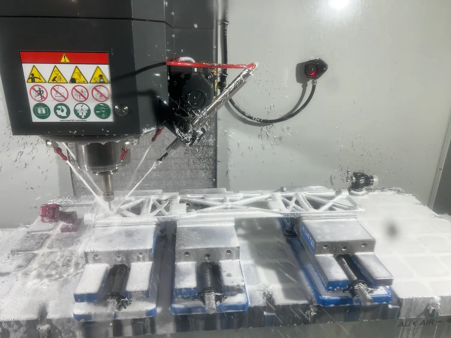 A CNC milling machine cutting a metal part held in vises, flooded with coolant, on the NCX Concepts shop floor in Charlotte, NC.